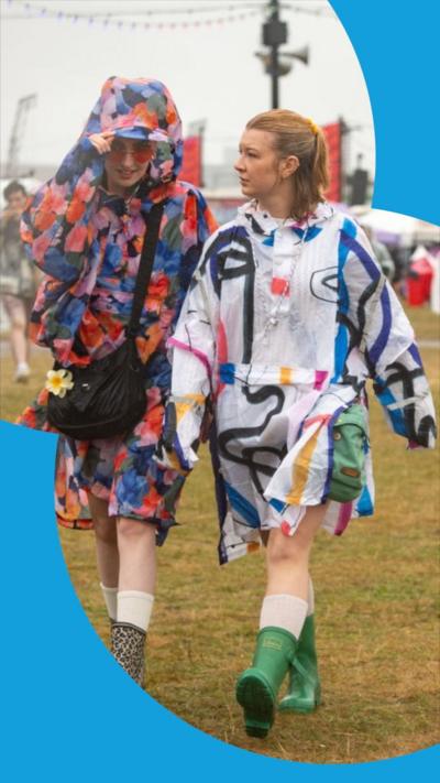 Two women wearing raincoats walk through festival site
