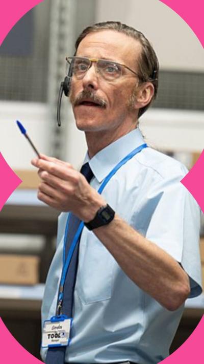 A man wearing a short-sleeved blue shirt holds up a pen in his right hand. He's wearing a tie, lanyard, and glasses.