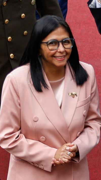 Delcy Rodriguez, standing smiling in a pale pink suit and wearing glasses