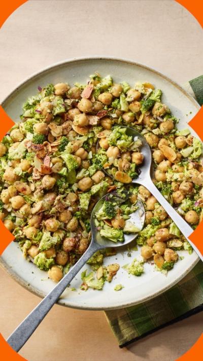 Aerial view of broccoli and chickpeas in a bowl with two spoons in it. It sits on a green checked napkin