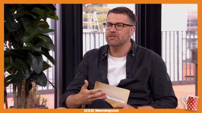 James Greenwood in the Morning Live studio with a white t shirt and black open shirt.