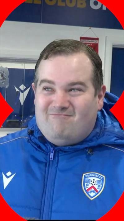 A man smiling in a blue football jacket.