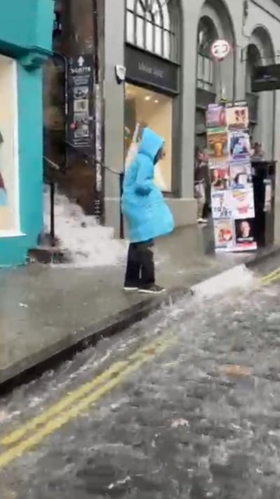 Woman in blue coat standing by cobbled street running with rain