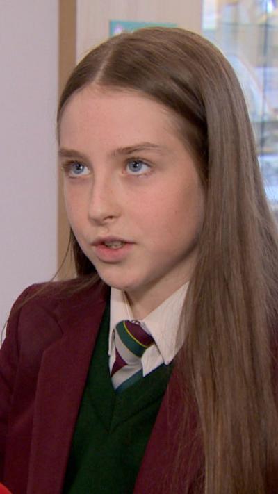 A girl with long brown hair and a maroon jacket looks off camera. 