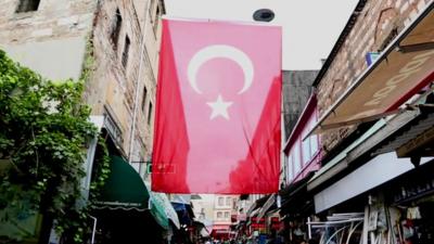 A flag flies above a street lined with shops