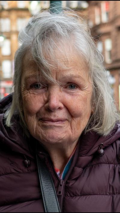 A woman with grey hair wearing a maroon jacket