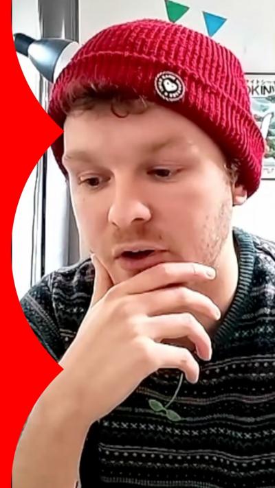 A man wearing a striped jumper and beanie hat rests his chin in his hand