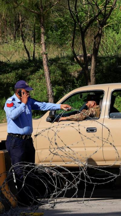A police officer removes barbed wire to make way for an army vehicle during patrols at the president's house, Islamabad, 19 April