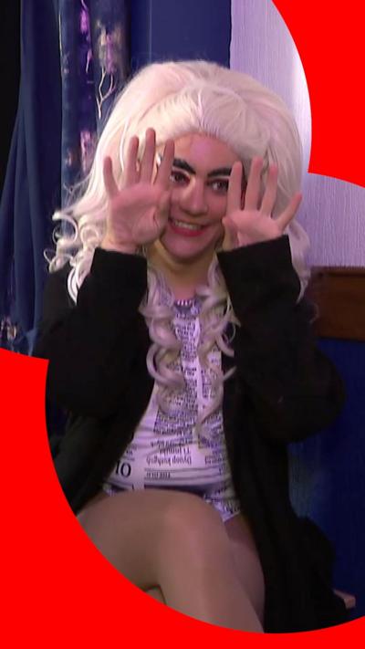 A drag queen with long blonde hair demonstrates 'flirting' in sign language - she holds up both hands
