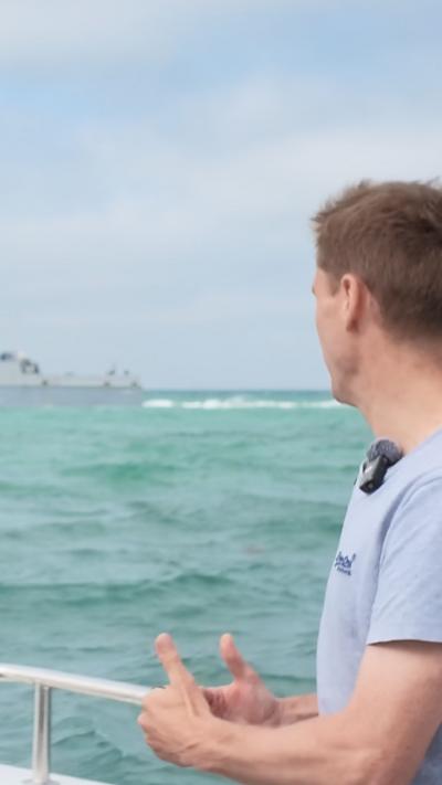 Chris Philp stood on a boat with the French navy patrol boat behind him