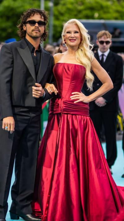 A man with shoulder-length dark hair, wearing sunglasses and a black suit. And a woman with long blonde hair wearing a red dress.
