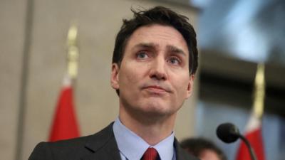 Justin Trudeau is seen behind a podium in a close up shot. He's wearing a grey suit, tie and blue shirt.