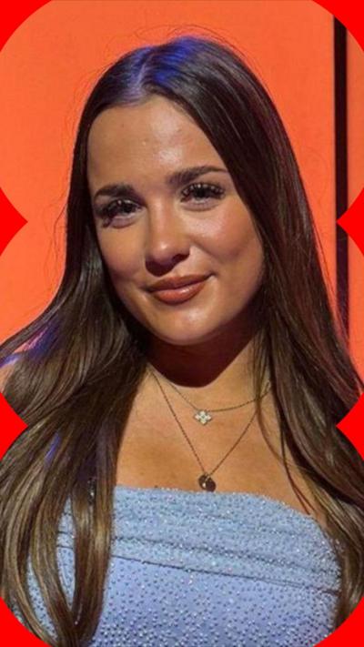 Sienna Mcswiggan has long brown hair and wears a light blue sleeveless top and two necklaces. She stands in front of an orange background 