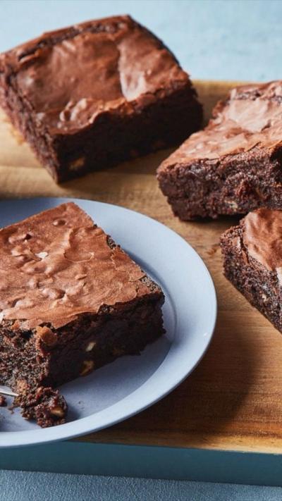 A chopping board with a stack of brownies on top. One is on a blue plate.