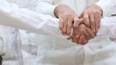 Close up of hands as Colombian president and FARC leader shake hands (with Cuban leader's hands holding both of them)