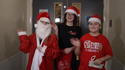 three children in festive outfits waving at camera