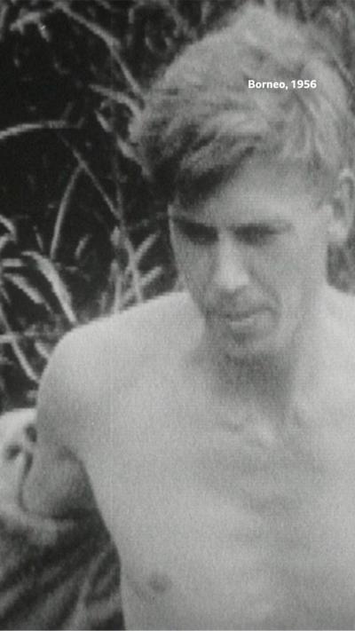 A close-up of Sir David Attenborough topless walking through a forest