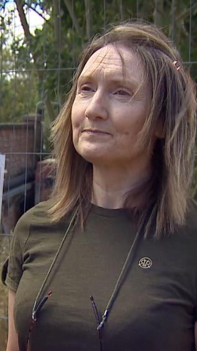 A woman with brown hair and a khaki t-shirt with glasses attached to a string around her neck