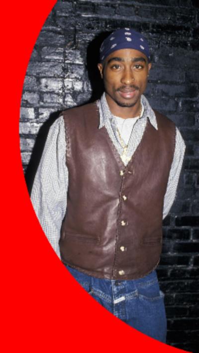 Image os Tupac Shakur wearing a blue bandana and a brown leather vest over a spotty white shirt.