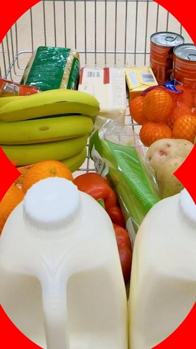 A close-up up shot of household groceries in a supermarket trolley, including milk, bananas, red peppers, potatoes, oranges, pasta, cheese, butter and canned goods.