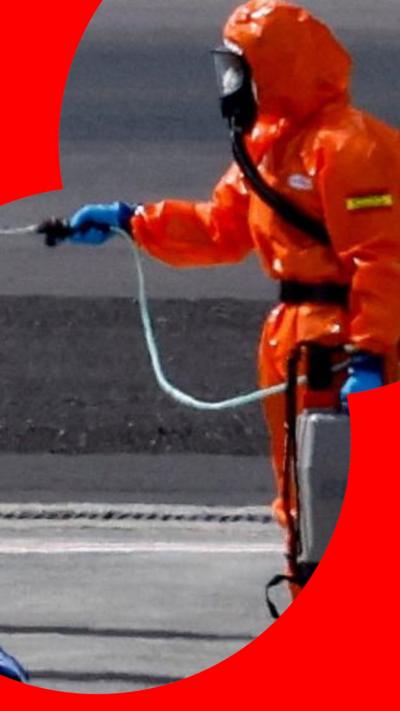 Someone in an orange protective suit sprays a fellow person in a protective suit 