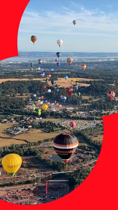 Dozens of colorful hot air balloons soaring above scenic countryside.