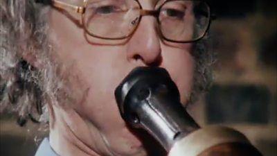 Close-up of a man's face blowing into a Renaissance woodwind instrument's mouthpiece