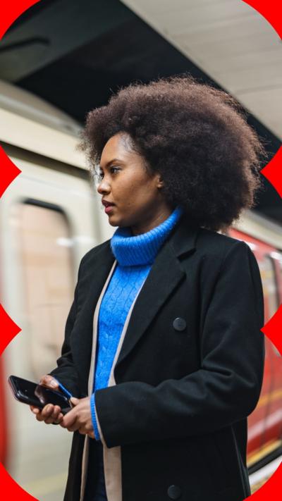 A woman stands on a Tube platform with her phone out.