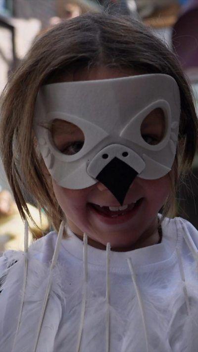 A girl wears a seagull mask and smiles into the camera