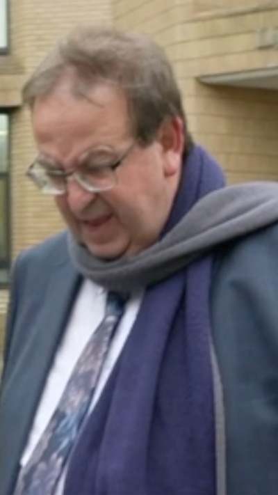 A man in his 50s in a suit and a purple and grey scarf with brown hair and glasses