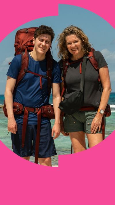 Dylan and Jackie in T-shirts and shorts pose on a sunny beach. They are both wearing backpacks