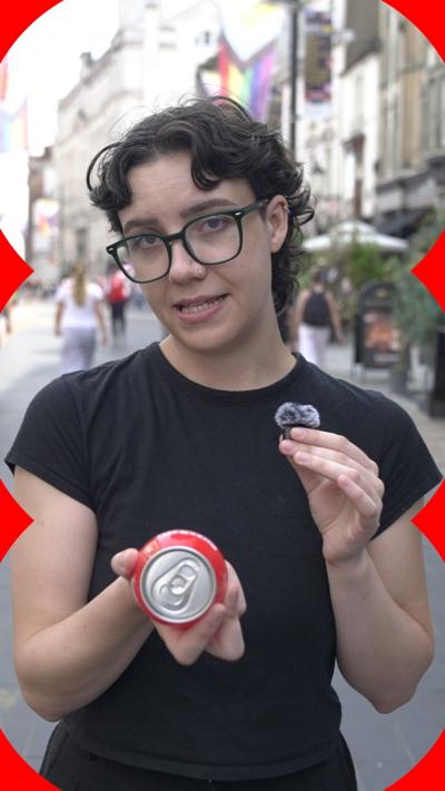 A person with short dark curly hair wearing a black t-shirt talks to the camera