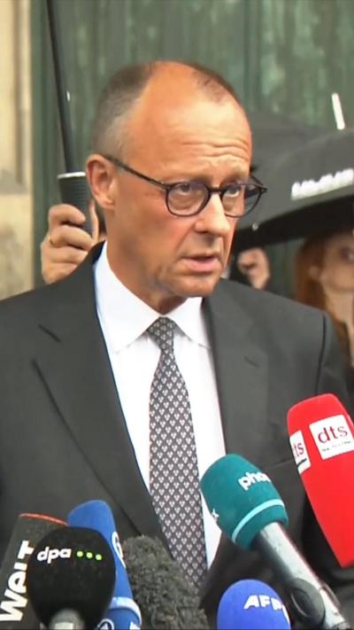 German chancellor in a suit speaking into microphones.