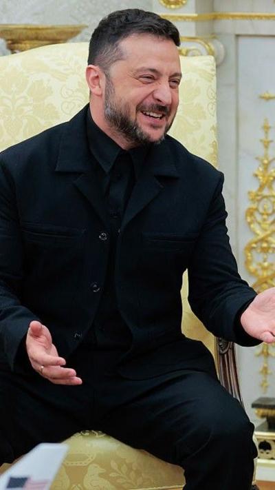 Zelensky in a black suit smiling in the Oval Office
