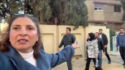 The BBC's Lina Sinjab pointing towards the house belonging to Bashar al-Assad with people walking in front of it