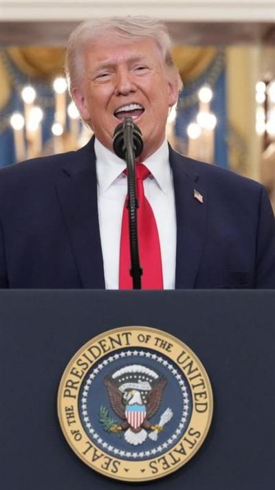 President Donald Trump, dressed in a blue suit and red tie, speaks into a microphone on a podium with the presidential seal.