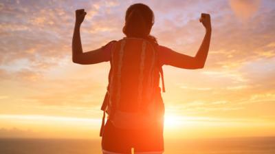 A person flexes their biceps and raises their fists towards a beautiful sunrise