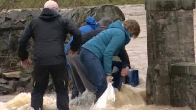 People attempting to block a gap in the wall to prevent floodwaters getting in