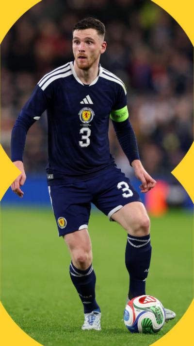 Andy Robertson has short dark hair and is wearing the Scotland national team football kit. he has a football at his feet during a game.
