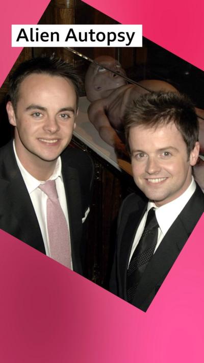 Ant and Dec wear black suits while standing in front of a model of an alien in a glass box