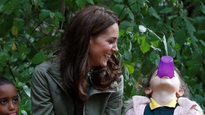 The Duchess of Cambridge sits next to a child playing with a cup