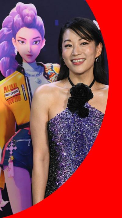 Pic of Arden Cho smiling and standing in front of a picture of her character, Rumi