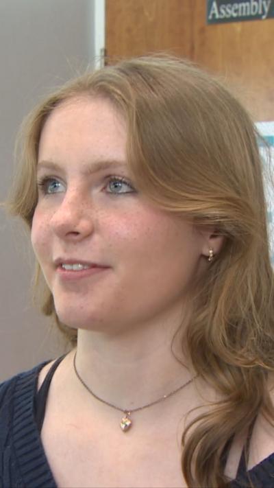A teenage girl with long fair hair who is wearing a dark blue top. She is looking off to the side. 
