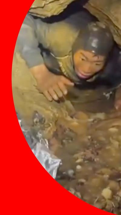 A man's head and arms emerge from a flooded cave with rescuers around him