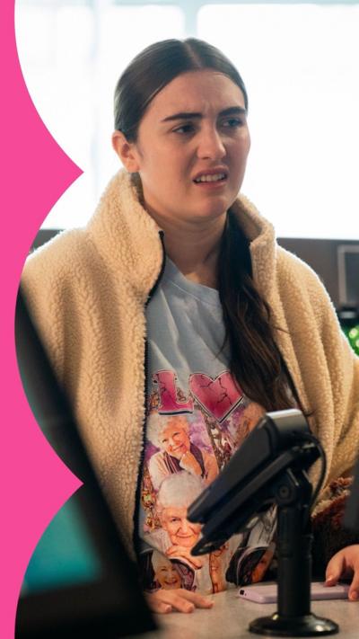 Woman with brown hair stands behind a shop counter with a card machine in view.