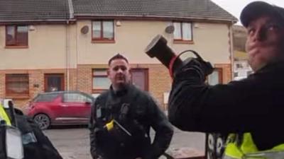 Three police officers on a street while one of them holds a battering ram above their head