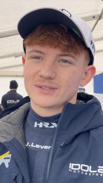 A racing driver in a blue outfit and white cap