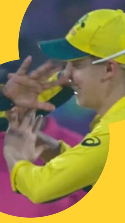 Hands near a face of a cricket player wearing a yellow and green hat.