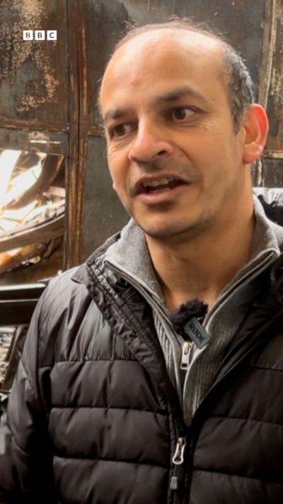 A balding man in a black coat and grey under jacket