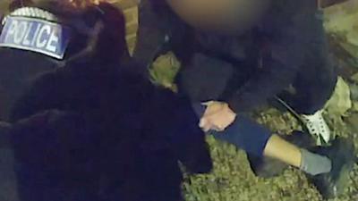 Two police officers surrounding a suspect on the ground. His leg is in the frame.